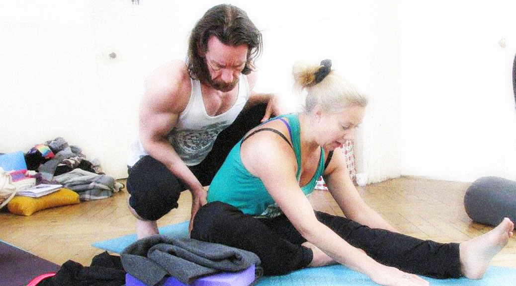 Mysore-style Ashtanga practice: a hands-on adjustment in a seated forward fold